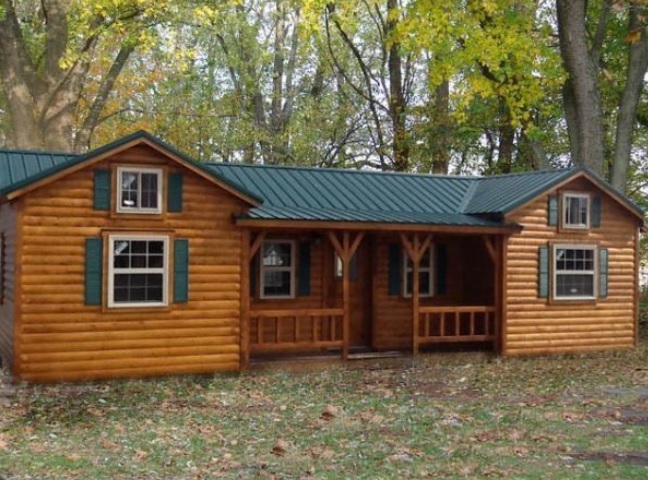 Beautiful one-story Amish log cabin with green shutters surrounded by trees